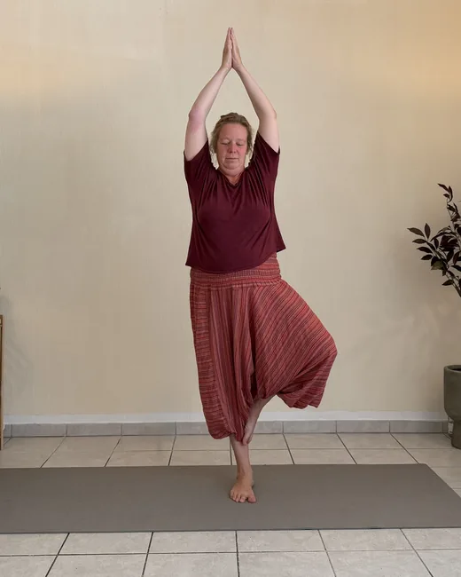Yogalehrerin in der Baumhaltung, die Hände über dem Kopf, zwischen zwei Stehlampen im Studio Sonnenaufgang