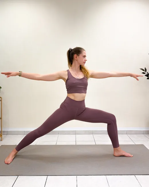 Yogalehrerin im Krieger II mit weit ausgestreckten Armen auf der Matte im Studio Sonnenaufgang